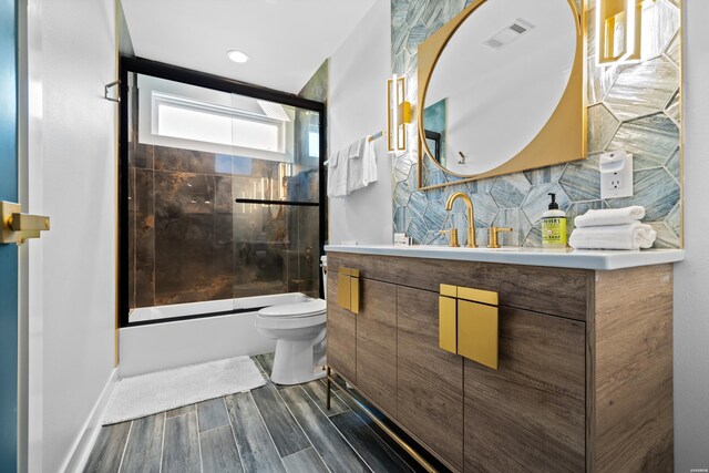 bathroom with toilet, visible vents, vanity, combined bath / shower with glass door, and wood tiled floor