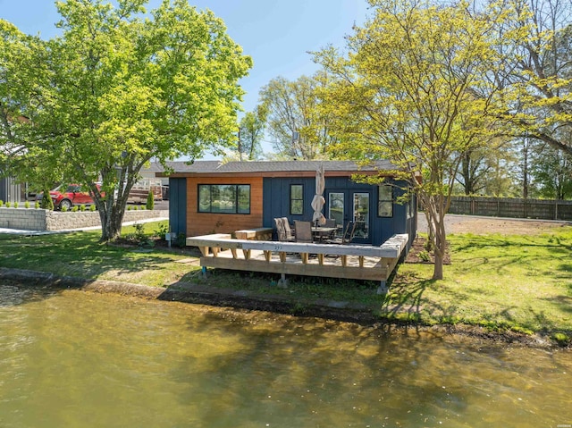 rear view of property with fence, french doors, a deck with water view, and a yard