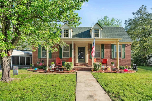 cape cod-style house featuring a shingled roof, brick siding, a front lawn, and covered porch
