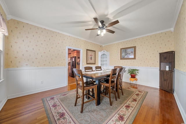 dining room featuring wainscoting, wood finished floors, ornamental molding, and a ceiling fan