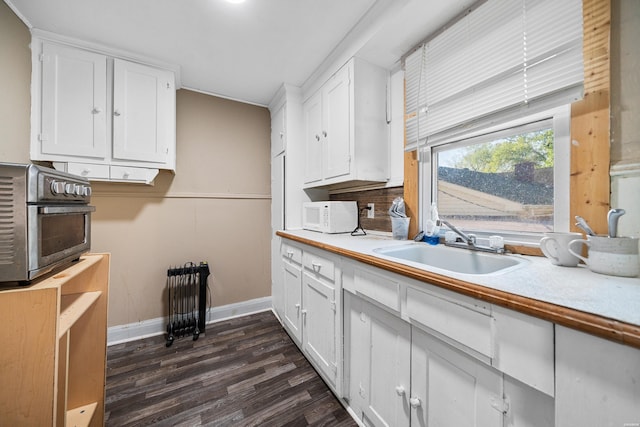 kitchen featuring white microwave, light countertops, white cabinets, dark wood finished floors, and a sink