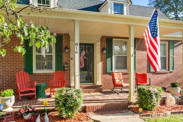 property entrance with roof with shingles, covered porch, and brick siding