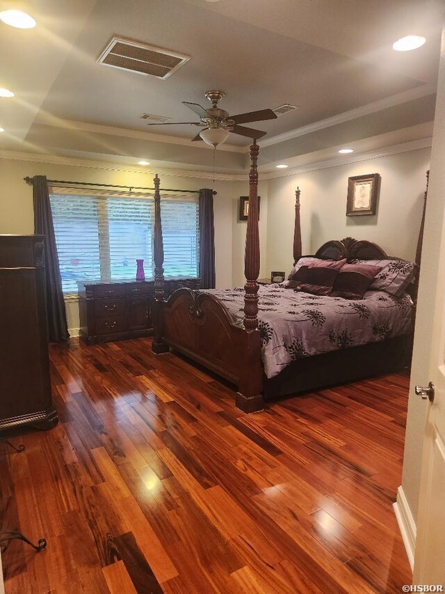 bedroom with dark wood-style floors, a tray ceiling, visible vents, and crown molding