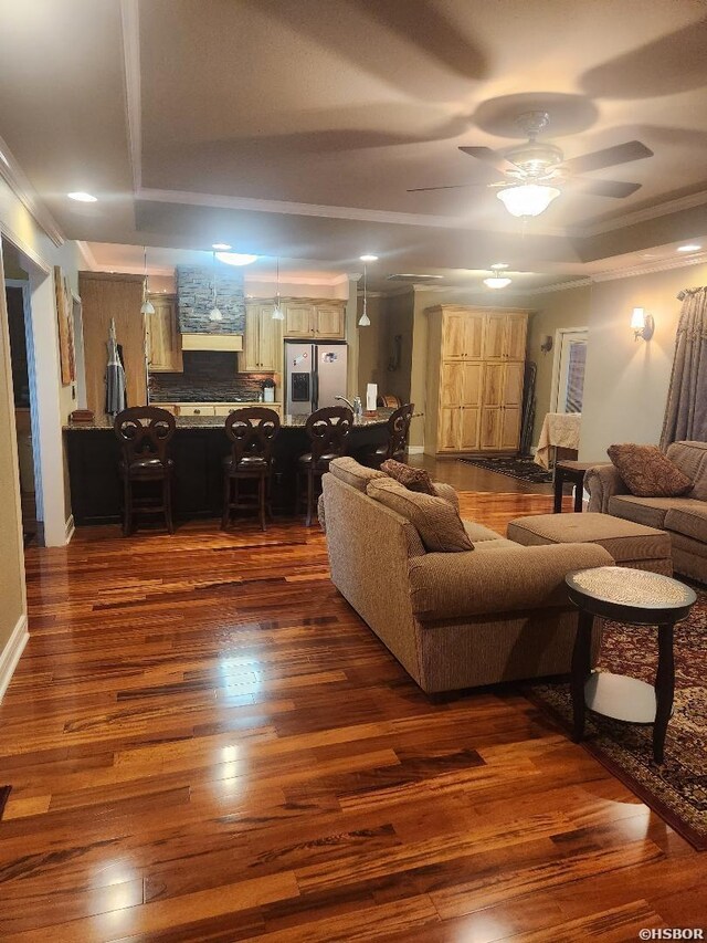 living room with a tray ceiling, dark wood-style flooring, crown molding, and ceiling fan