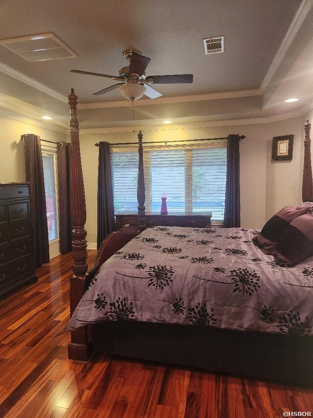 bedroom featuring a tray ceiling, crown molding, visible vents, and dark wood-style flooring