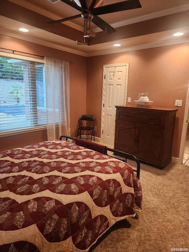 bedroom with a ceiling fan, a tray ceiling, crown molding, and carpet flooring