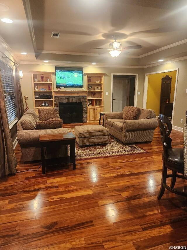 living area with a fireplace, wood finished floors, visible vents, a ceiling fan, and ornamental molding