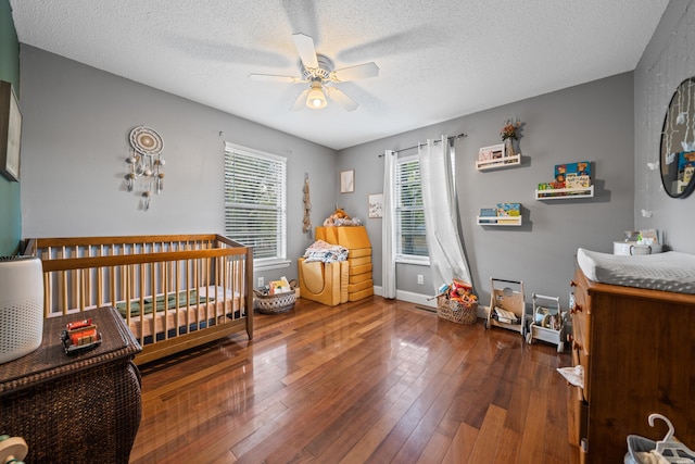 bedroom with a crib, baseboards, a textured ceiling, a ceiling fan, and wood-type flooring