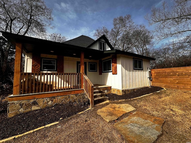 view of front of home with a porch, a shingled roof, and fence