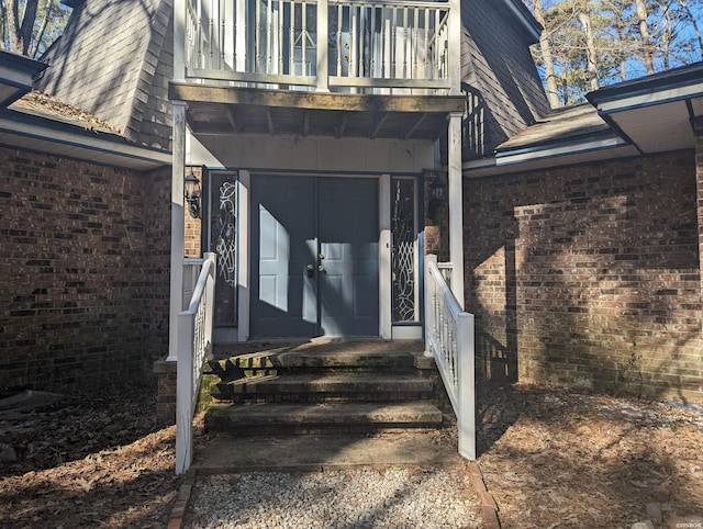 view of exterior entry with brick siding, board and batten siding, and a balcony