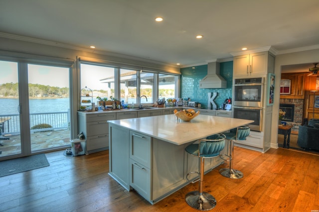 kitchen with custom range hood, a center island, a water view, stainless steel double oven, and a sink