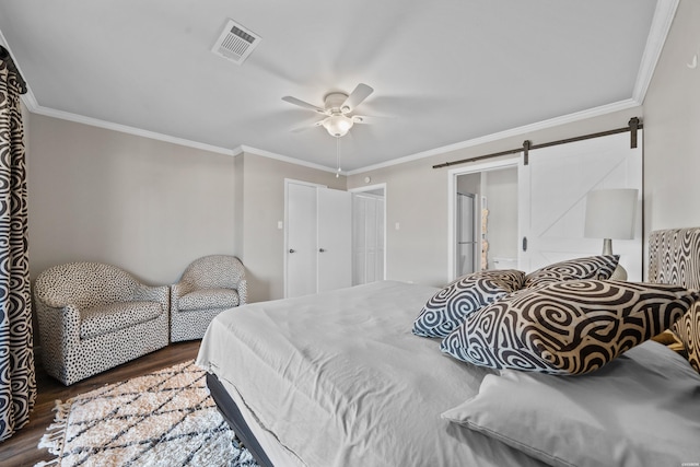 bedroom featuring visible vents, a barn door, ornamental molding, a ceiling fan, and wood finished floors