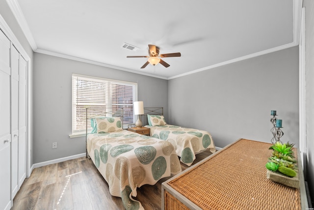 bedroom featuring wood finished floors, visible vents, baseboards, a closet, and crown molding