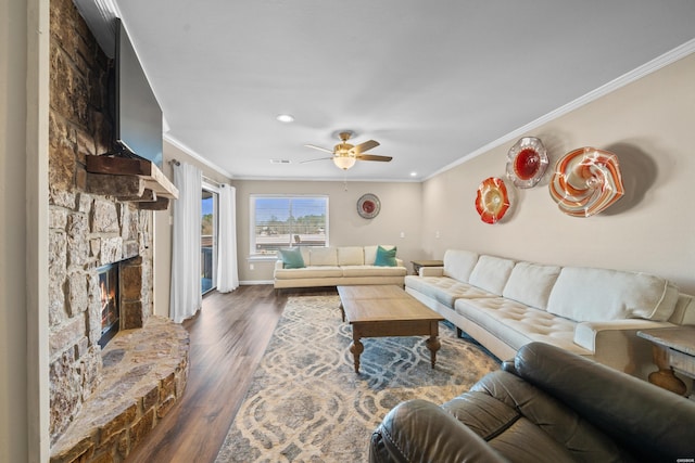 living room with ceiling fan, a stone fireplace, dark wood-style flooring, visible vents, and ornamental molding