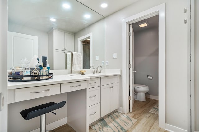 bathroom featuring baseboards, toilet, recessed lighting, wood finished floors, and vanity