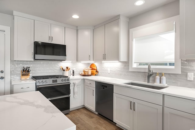 kitchen featuring recessed lighting, wood finished floors, light stone counters, appliances with stainless steel finishes, and a sink