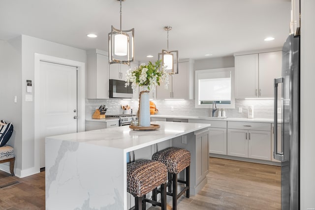 kitchen with a sink, decorative backsplash, stainless steel appliances, light wood-style floors, and a kitchen island