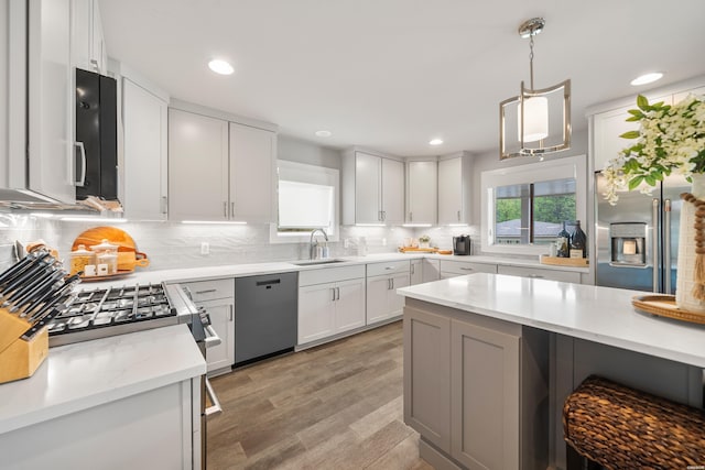 kitchen featuring tasteful backsplash, hanging light fixtures, light wood-style flooring, appliances with stainless steel finishes, and a sink