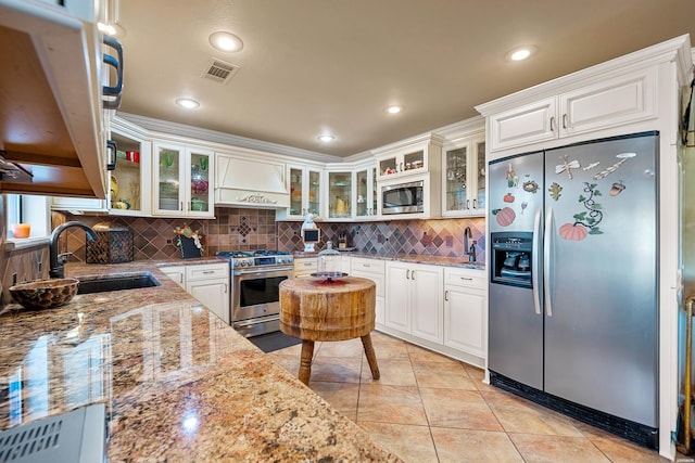 kitchen with appliances with stainless steel finishes, a sink, white cabinets, and custom range hood