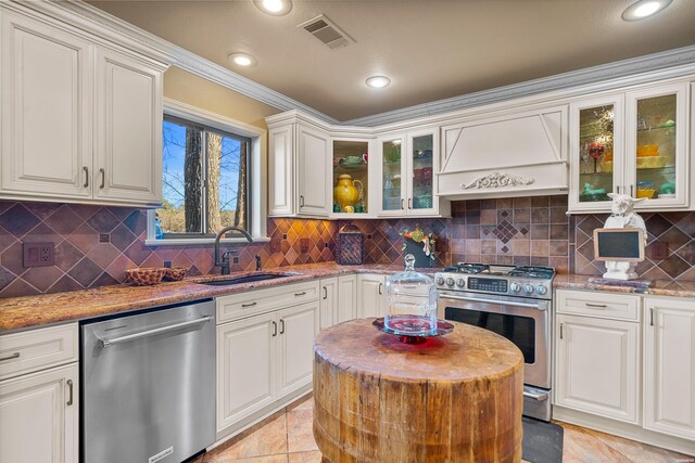 kitchen with premium range hood, a sink, white cabinetry, appliances with stainless steel finishes, and glass insert cabinets