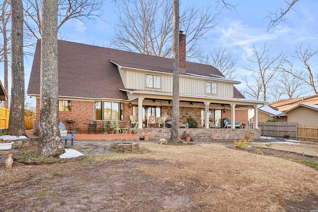 rear view of house with brick siding, board and batten siding, a patio area, ceiling fan, and fence