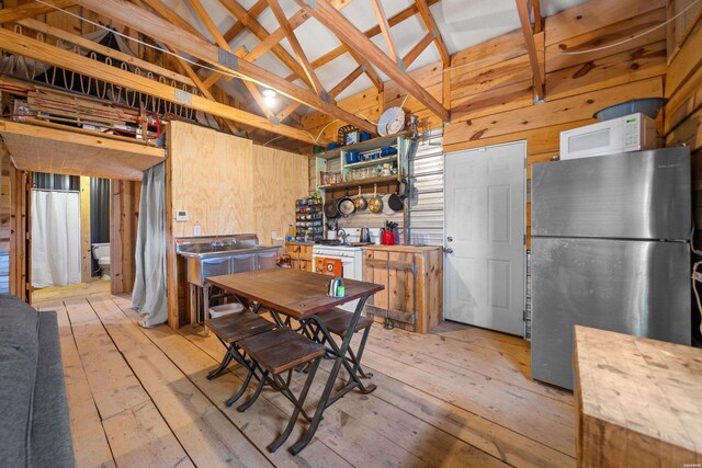 kitchen featuring white microwave, wooden walls, vaulted ceiling, and freestanding refrigerator