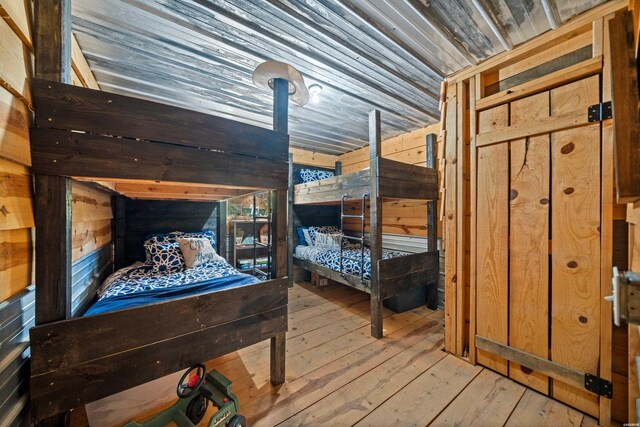 bedroom with lofted ceiling, wooden ceiling, light wood finished floors, and wood walls