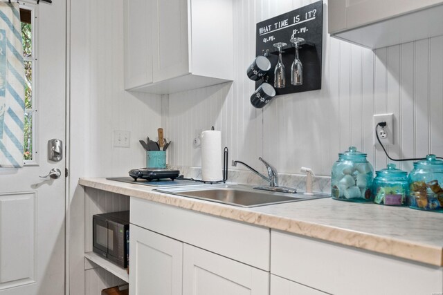 kitchen with light stone counters, black microwave, white cabinetry, and a sink