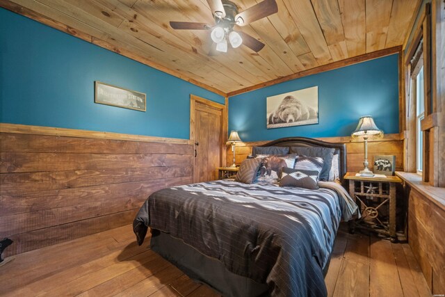 bedroom with ceiling fan, wooden walls, wood ceiling, light wood-style floors, and wainscoting