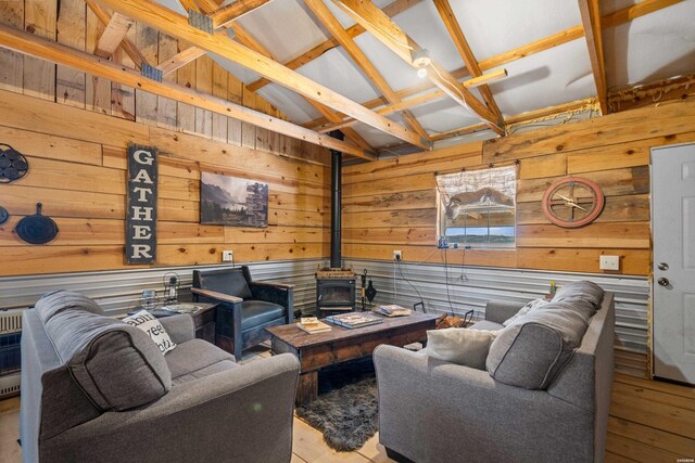 living area featuring vaulted ceiling with beams, light wood-style flooring, wood walls, and a wood stove