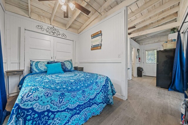 bedroom featuring lofted ceiling with beams, a ceiling fan, freestanding refrigerator, wood finished floors, and wooden ceiling