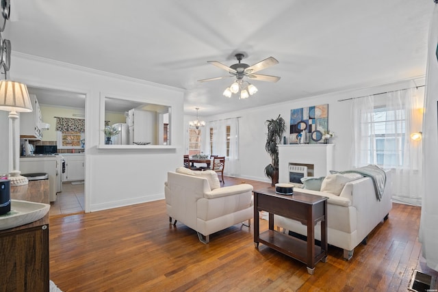 living room featuring visible vents, a glass covered fireplace, ornamental molding, wood finished floors, and ceiling fan with notable chandelier