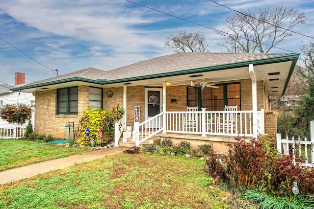 view of front of house featuring a porch, roof with shingles, fence, a front lawn, and brick siding