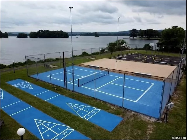 view of community featuring a water view, a tennis court, shuffleboard, and fence