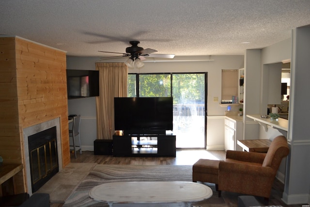 living area featuring a ceiling fan, a fireplace, a textured ceiling, and wood finished floors