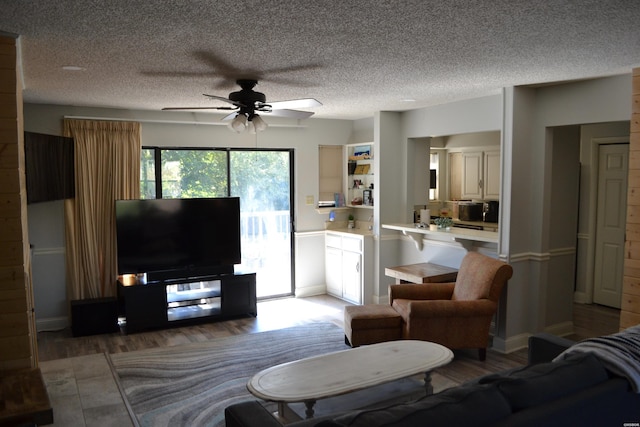 living area with ceiling fan, a textured ceiling, and dark wood-style flooring