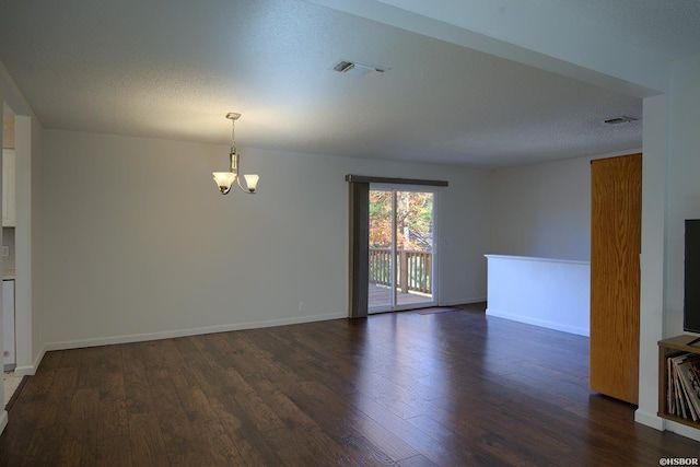 spare room with dark wood finished floors, visible vents, an inviting chandelier, a textured ceiling, and baseboards