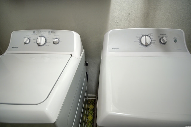 clothes washing area with a textured wall, separate washer and dryer, and laundry area