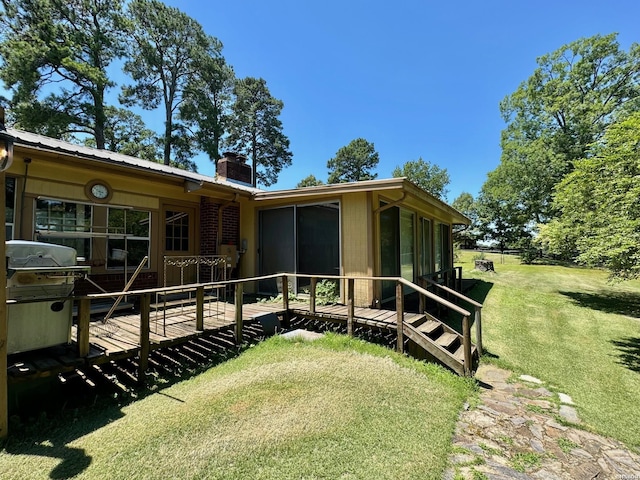 view of side of property with a lawn, a sunroom, a chimney, a deck, and brick siding