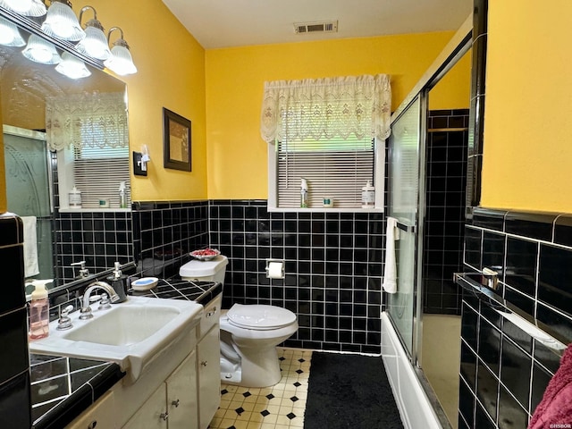 full bath with tile walls, visible vents, toilet, combined bath / shower with glass door, and vanity