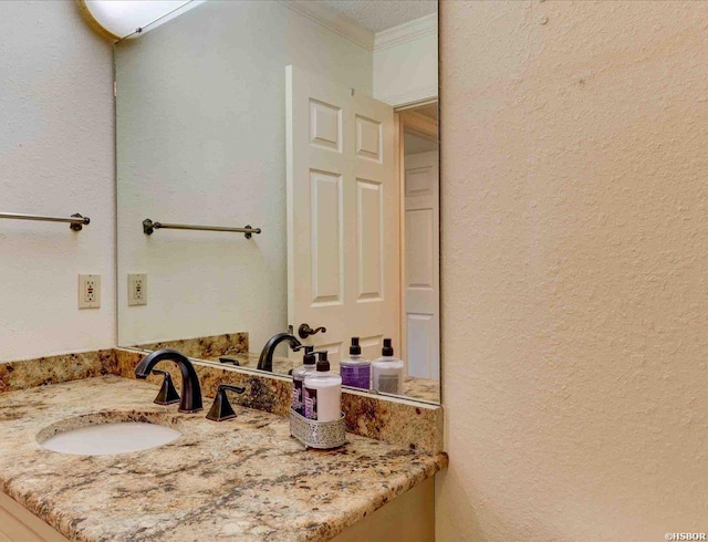 bathroom with a textured wall, crown molding, and vanity