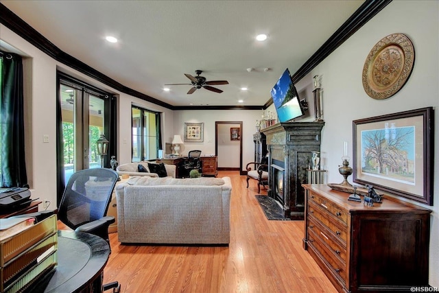 living area with a premium fireplace, crown molding, ceiling fan, and light wood-type flooring