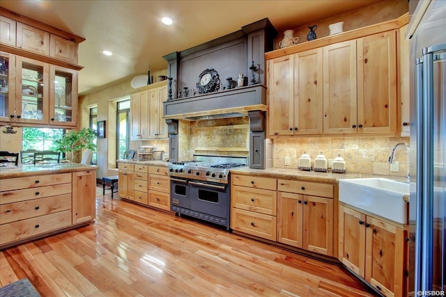 kitchen featuring decorative backsplash, light countertops, light brown cabinetry, and double oven range