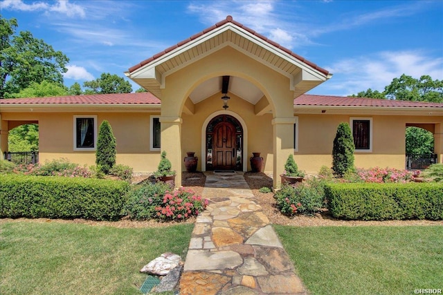 property entrance with stucco siding, a tiled roof, and a yard