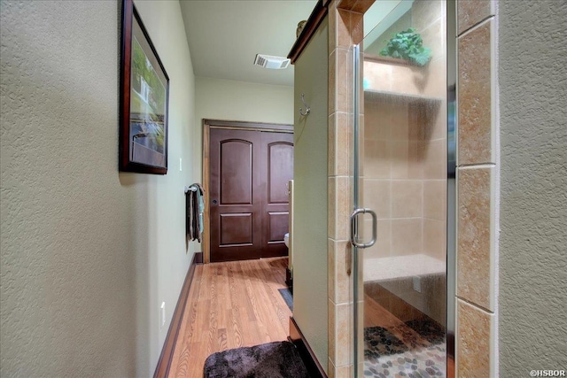 bathroom with a textured wall, visible vents, a shower stall, and wood finished floors