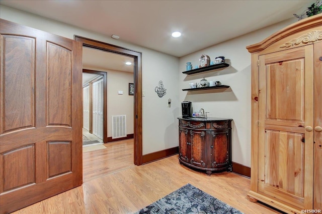 hall featuring baseboards, visible vents, and light wood finished floors