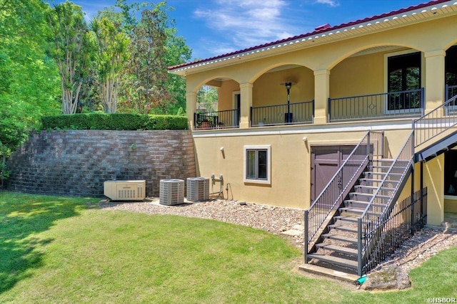 rear view of house featuring a yard, stucco siding, stairway, and central air condition unit