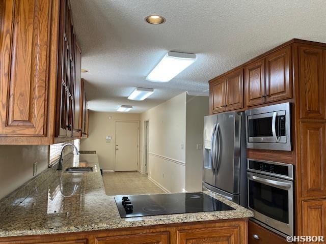 kitchen with a sink, brown cabinetry, stone counters, and stainless steel appliances