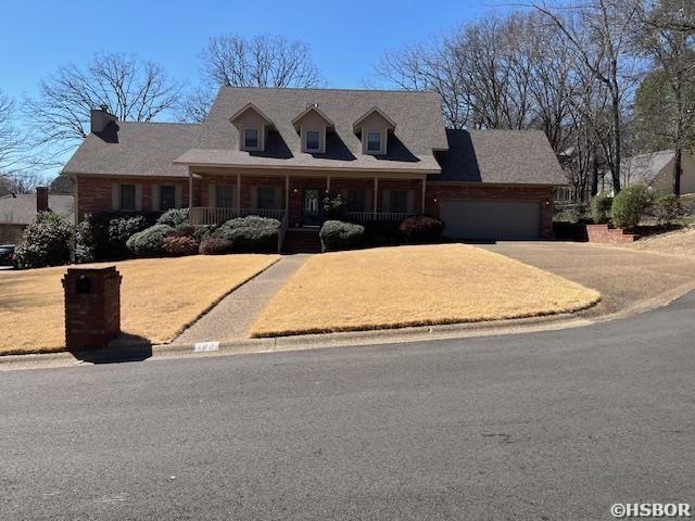 new england style home with covered porch, concrete driveway, and an attached garage