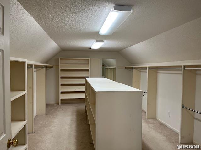 spacious closet with lofted ceiling and light colored carpet